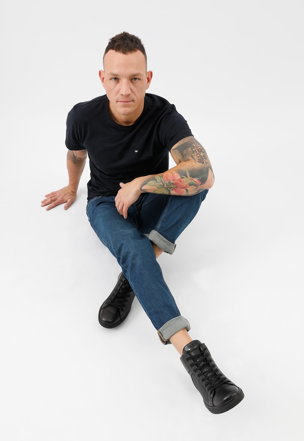 Czarne trampki męskie Wojas model 24026-71 z tłoczonymi elementami, prezentowane na nogach w podwiniętych jeansach, widok z boku pokazujący wysoki krój obuwia.