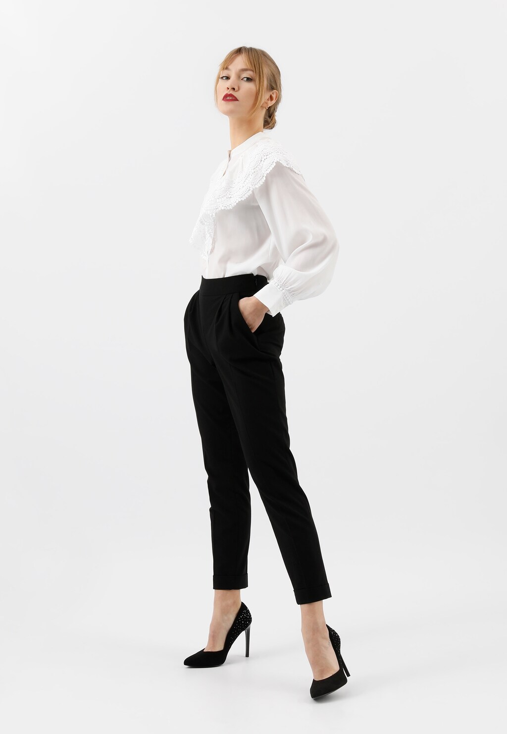 Eleganckie czarne czółenka damskie Wojas model 9350-61 z błyszczącymi dżetami na tyle buta, na wysokim szpilkowym obcasie, widoczne na nodze osoby w czarnych spodniach.