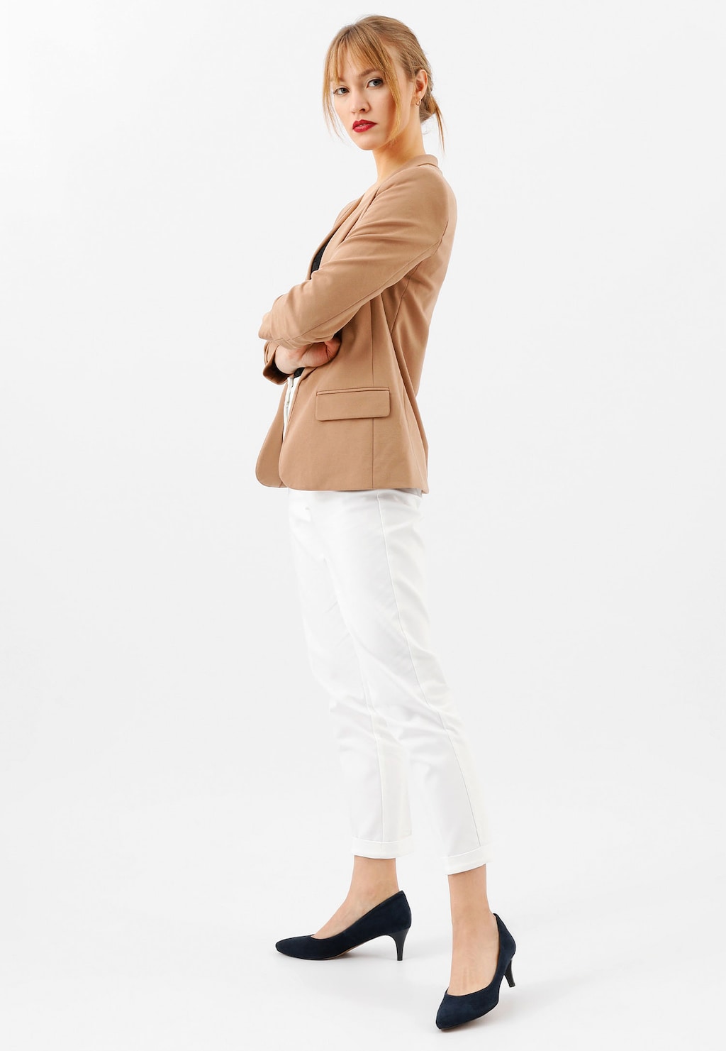 Kobieta w beżowym żakiecie i białych spodniach prezentująca granatowe czółenka Wojas model 35035-66 na średnim obcasie, widok z boku.