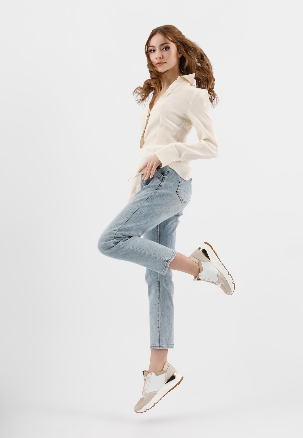 Modelka w jasnej koszuli i jasnoniebieskich jeansach prezentuje białe sznurowane sneakersy damskie Wojas model 46137-89 w kolorze biało-beżowym, stojąc na jednej nodze w dynamicznej pozie.