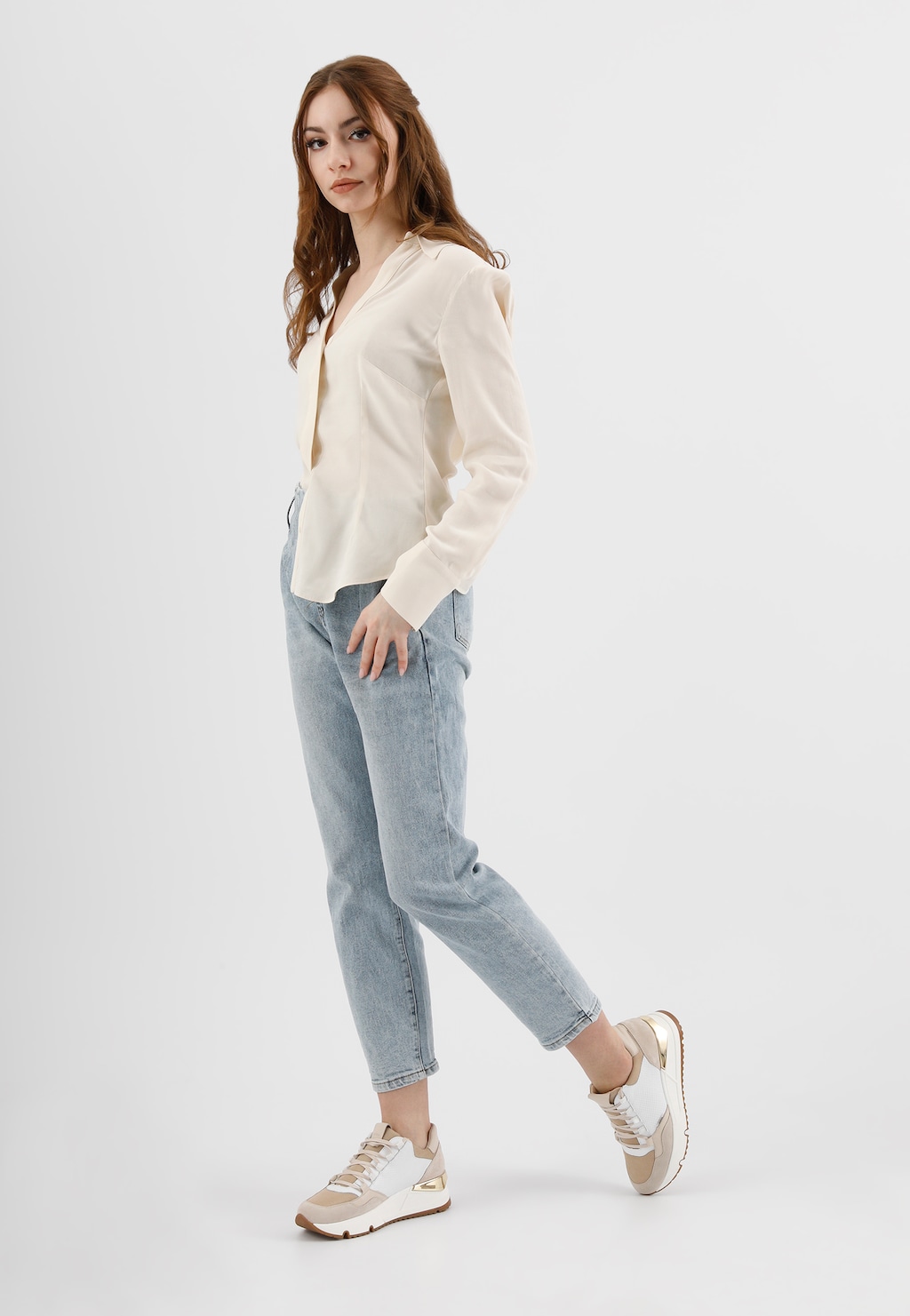 Modelka w jasnej bluzce i jasnoniebieskich jeansach prezentuje sznurowane sneakersy Wojas model 46137-89 w biało-beżowej kolorystyce, idealne do casualowych stylizacji.