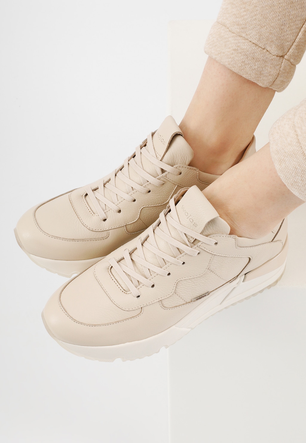 Skórzane sneakersy damskie Wojas model 46136-54 w kolorze beżowym na stopach w lekkich spodniach. Widok z góry na buty o sportowym kroju z wyraźnymi przeszyciami.