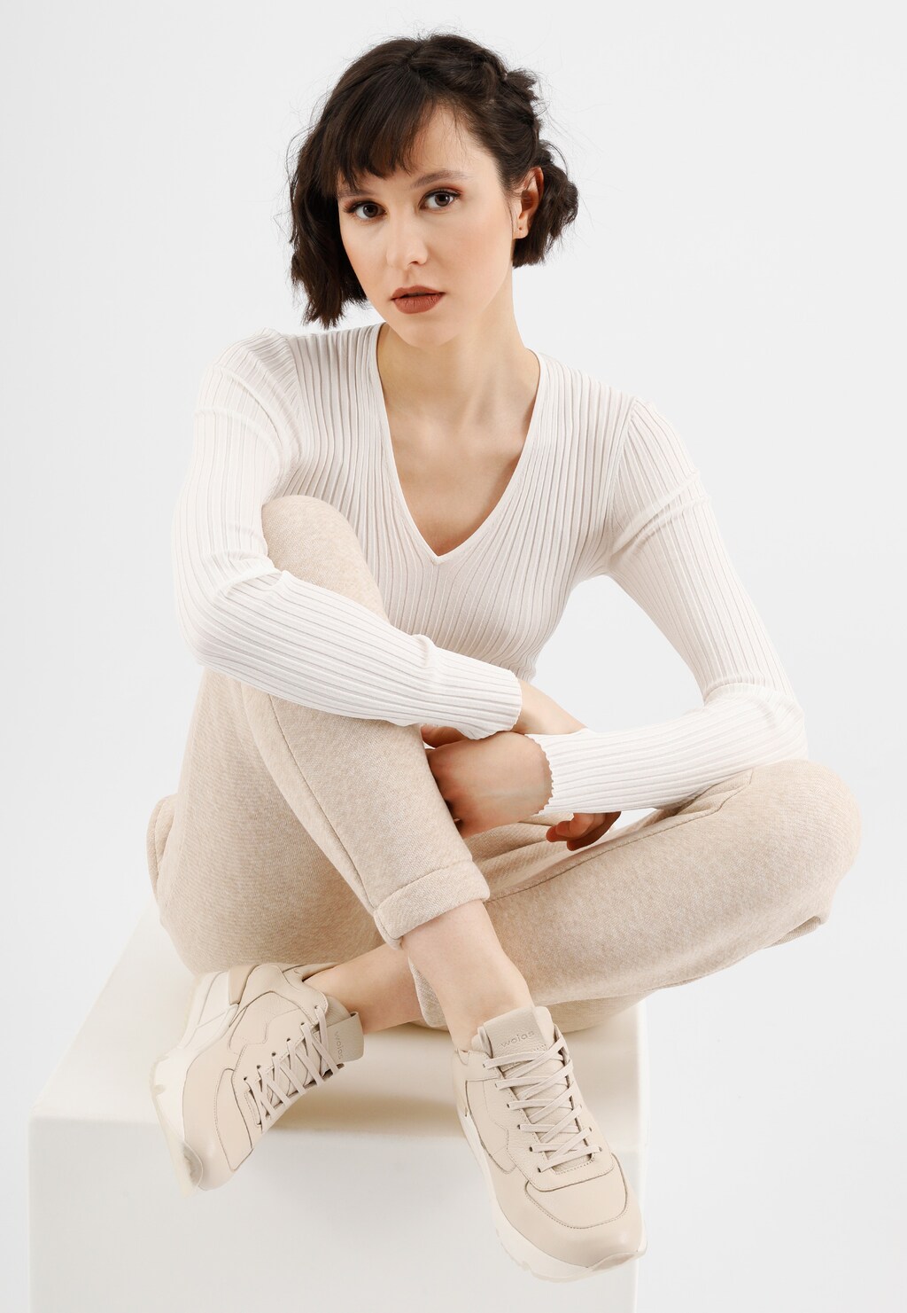 Eleganckie beżowe sneakersy Wojas model 46136-54 ze skóry, zaprezentowane na osobie w jasnym stroju, siedzącej w minimalistycznej stylizacji.