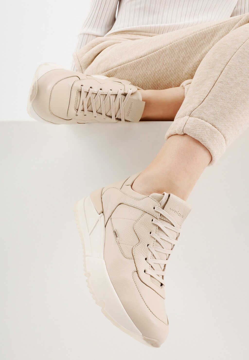 Beżowe skórzane sneakersy damskie Wojas model 46136-54 prezentowane na nogach osoby w jasnych spodniach, ukazujące sportowy design z charakterystycznymi sznurówkami.