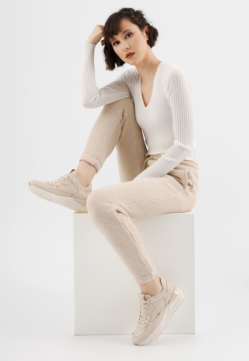 Beżowe skórzane sneakersy damskie Wojas model 46136-54 prezentowane na modelce w jasnym stroju, siedzącej na białym podeście w eleganckiej stylizacji.