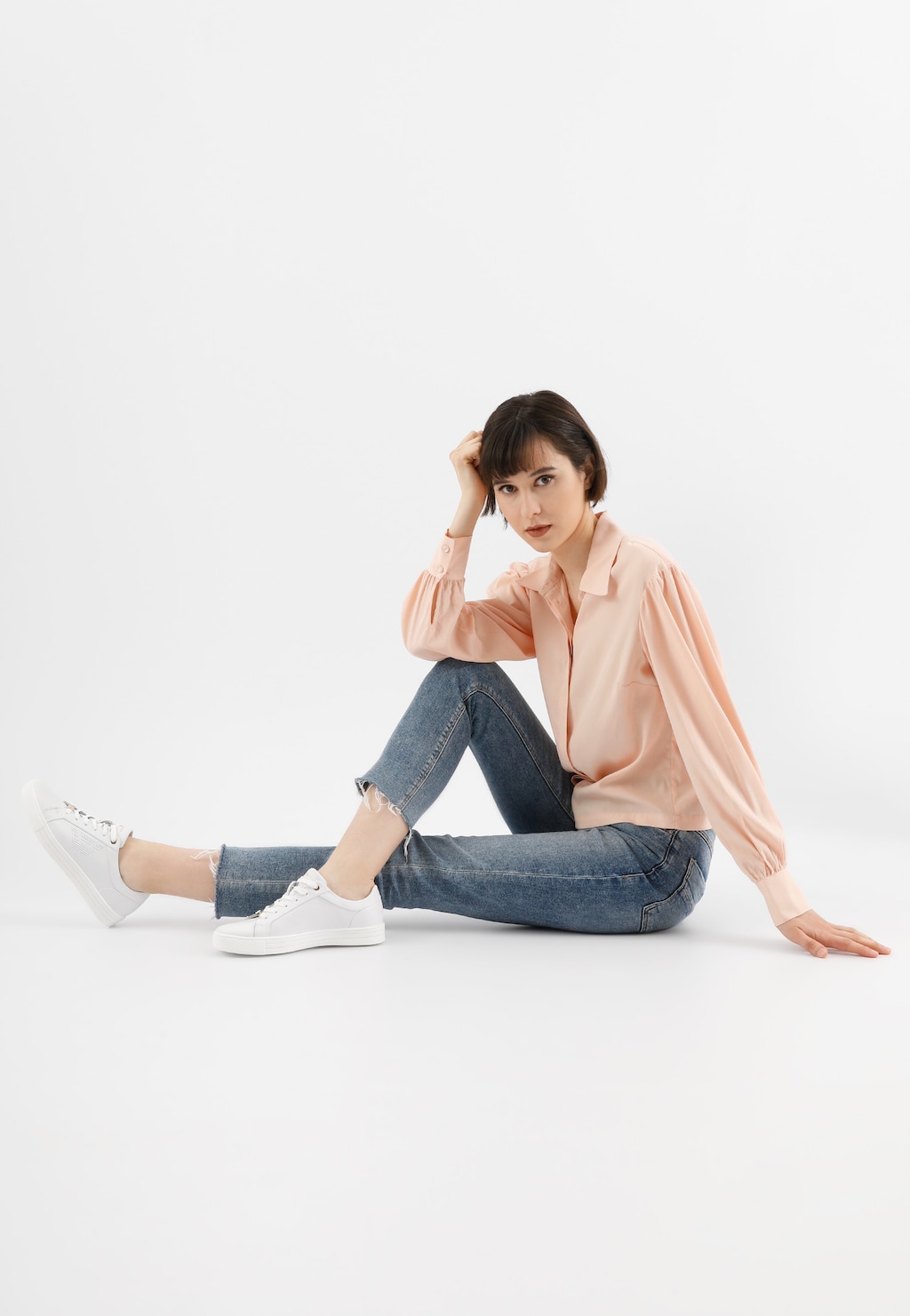 Osoba w modnej stylizacji z białymi półbutami Wojas 46084-59 z dziurkowanym logo, w połączeniu z jeansami i pastelową koszulą w pozycji siedzącej.