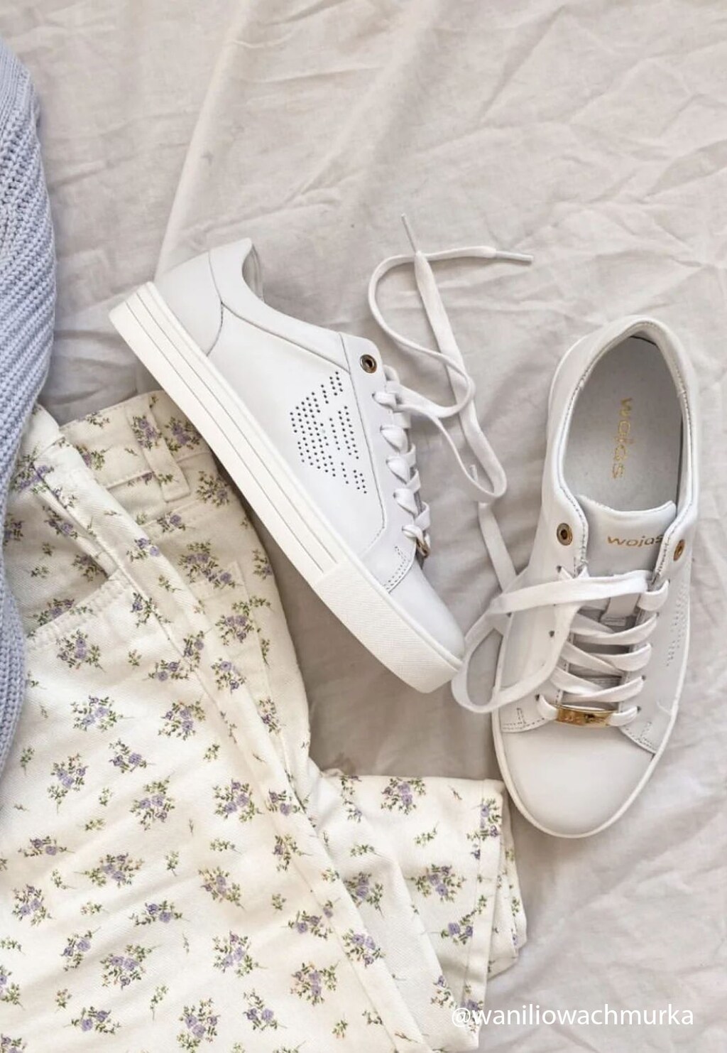 Białe półbuty damskie Wojas model 46084-59 z charakterystycznym dziurkowanym logo, sznurowane, na płaskiej podeszwie, ukazane w stylizacji z kwiecistą spódnicą.