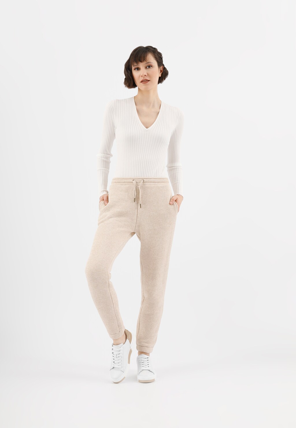 Stylizacja z białymi trampkami Wojas model 46121-54 z beżowymi akcentami, biały sweter z dekoltem w serek i beżowe dresowe spodnie, tworząc elegancki casualowy look.