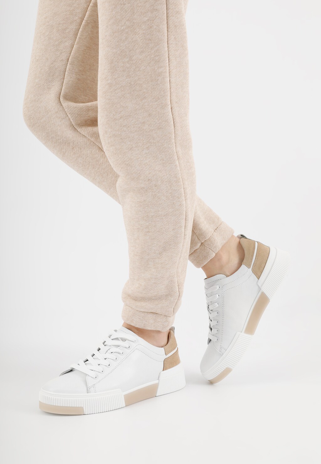 Białe trampki damskie Wojas model 46121-54 z beżowymi wstawkami, noszone do jasnobeżowych spodni. Widok z boku ukazujący eleganckie połączenie sportowego obuwia z casualowym stylem.