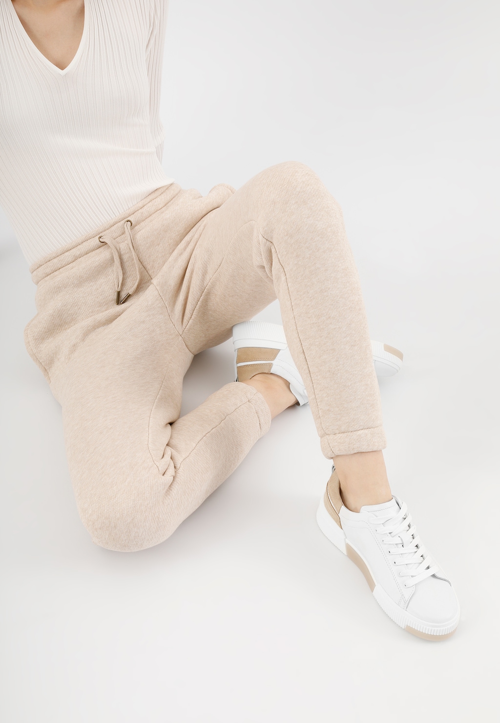 Białe trampki damskie Wojas model 46121-54 z beżowymi akcentami na nodze osoby ubranej w jasnobeżowe spodnie dresowe, widok z boku pokazujący stylowy sportowy look.