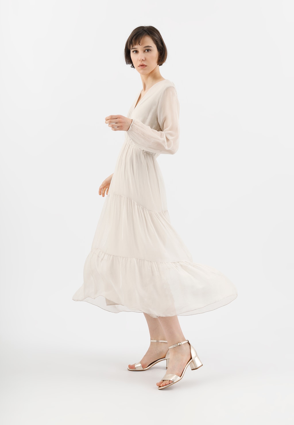 Elegancka osoba w kremowej sukni prezentująca złote sandały damskie Wojas model 76051-58 na średnim obcasie, z delikatnym zapięciem na kostce.