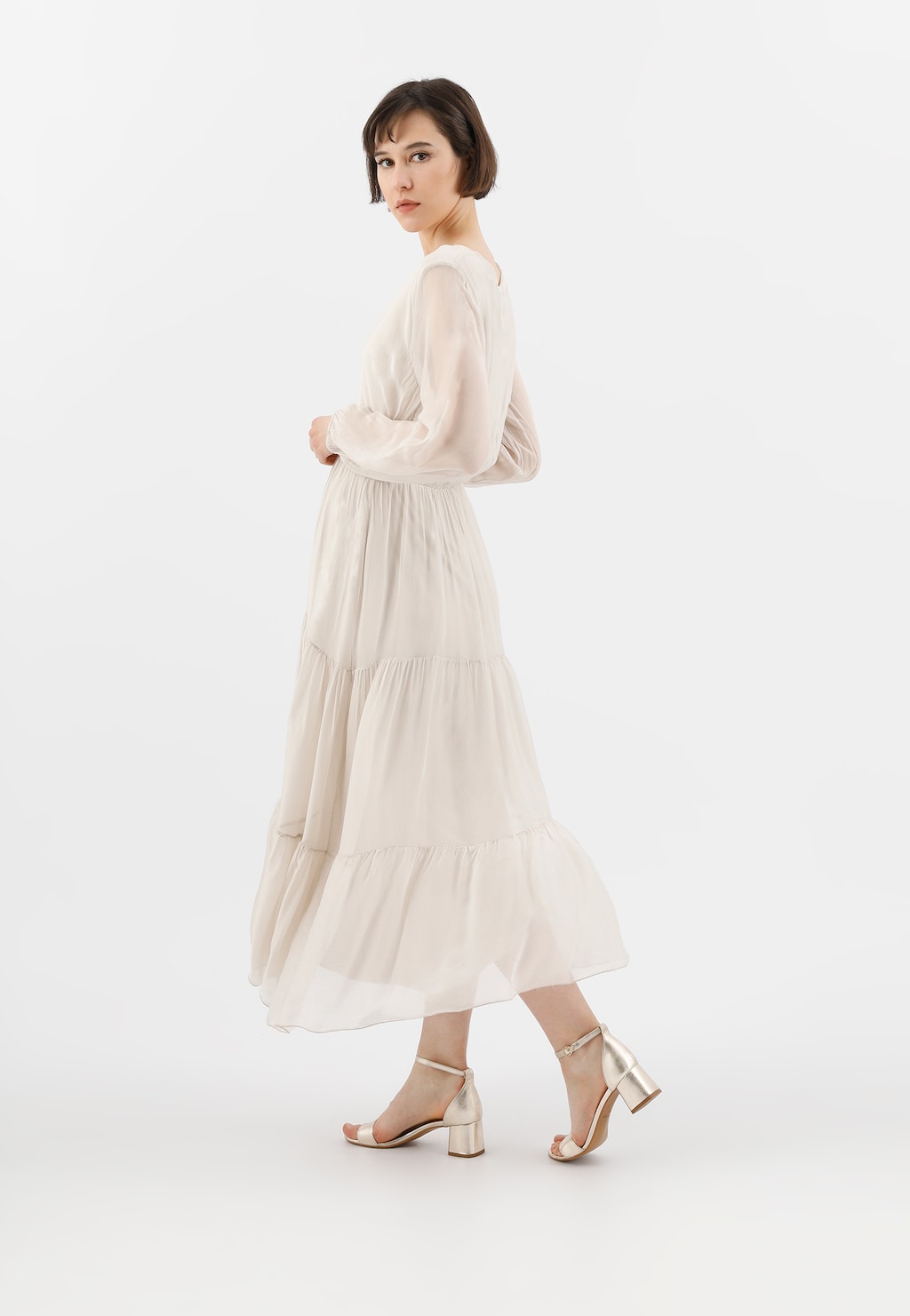 Modelka w długiej, kremowej sukience z tiulu prezentuje złote sandały damskie Wojas model 76051-58 na niskim obcasie, idealne do eleganckich letnich stylizacji.