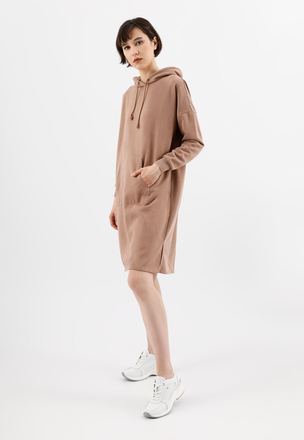 Kobieta w beżowej sukience z kapturem typu hoodie, prezentująca białe sneakersy damskie Wojas model 46115-79 na podwyższonej podeszwie.