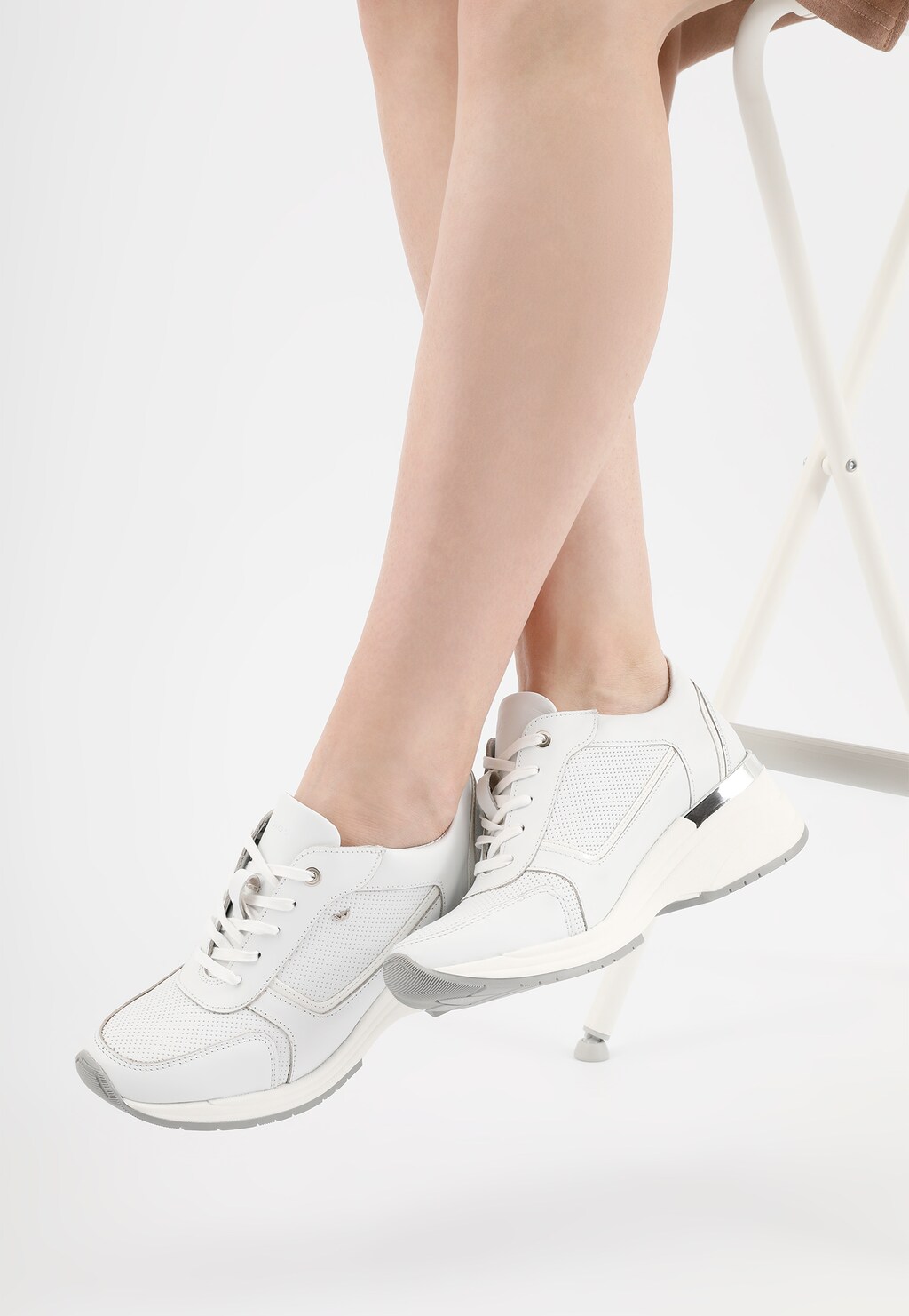 Białe sneakersy damskie Wojas model 46115-79 na podwyższonej podeszwie, prezentowane na nogach modelki, z perforowanymi elementami i szarymi detalami na podeszwie.