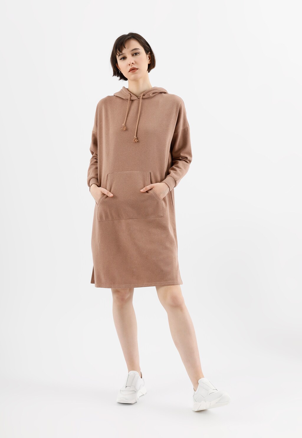 Kobieta w beżowej sukience z kapturem, prezentująca białe sneakersy wsuwane Wojas model 46119-59 na grubej podeszwie, idealne do casualowych stylizacji.