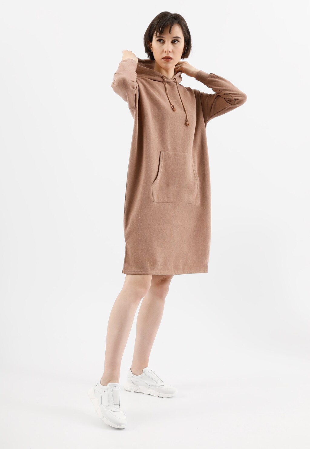 Kobieta w beżowej sukience z kapturem i kieszenią, ubrana w białe sneakersy Wojas model 46119-59 na grubej podeszwie, w casualowej pozie.