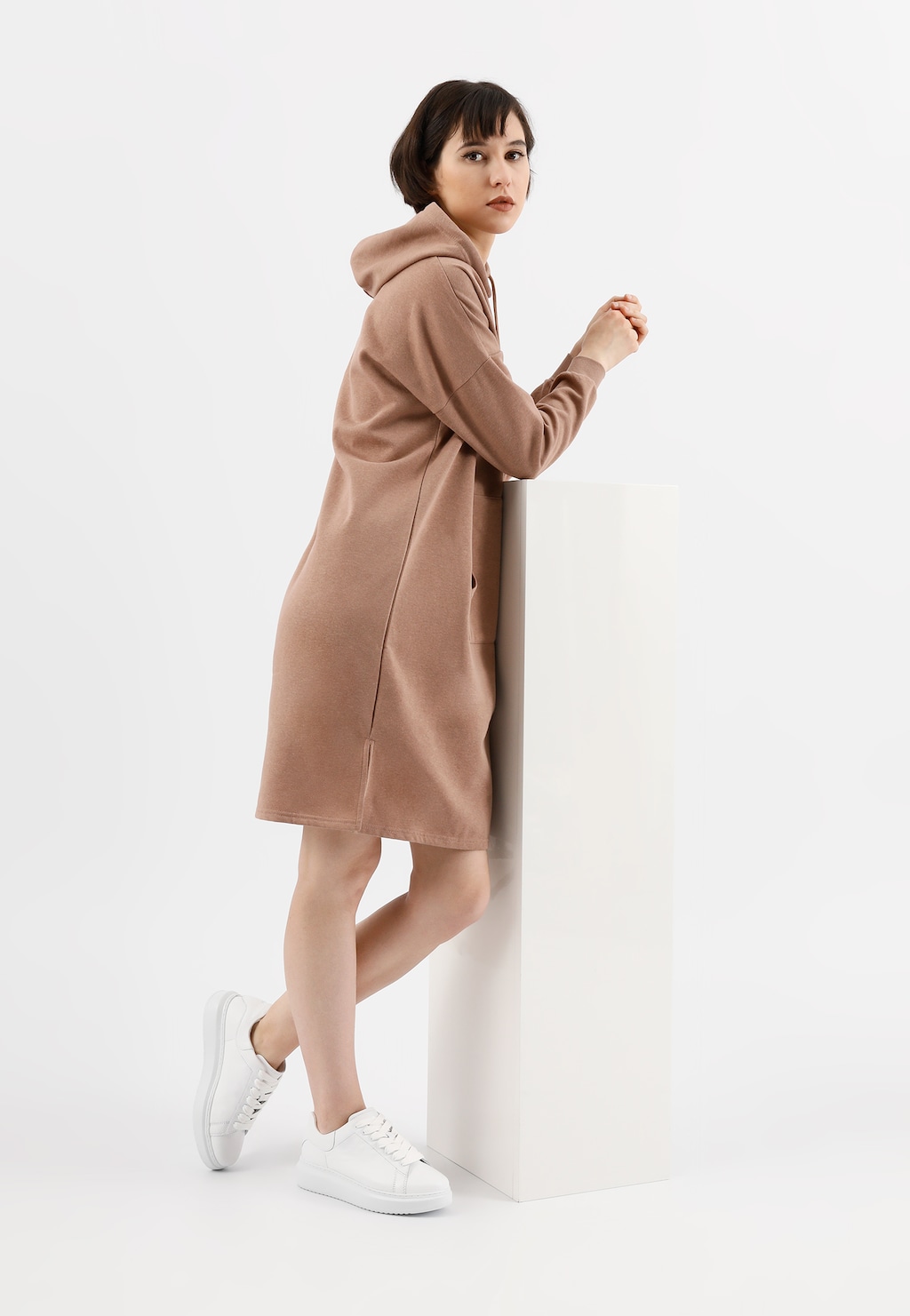 Modelka w beżowym płaszczu z kapturem prezentuje klasyczne białe trampki Wojas model 46020-50 wykonane ze skóry licowej, idealne do casualowych stylizacji.