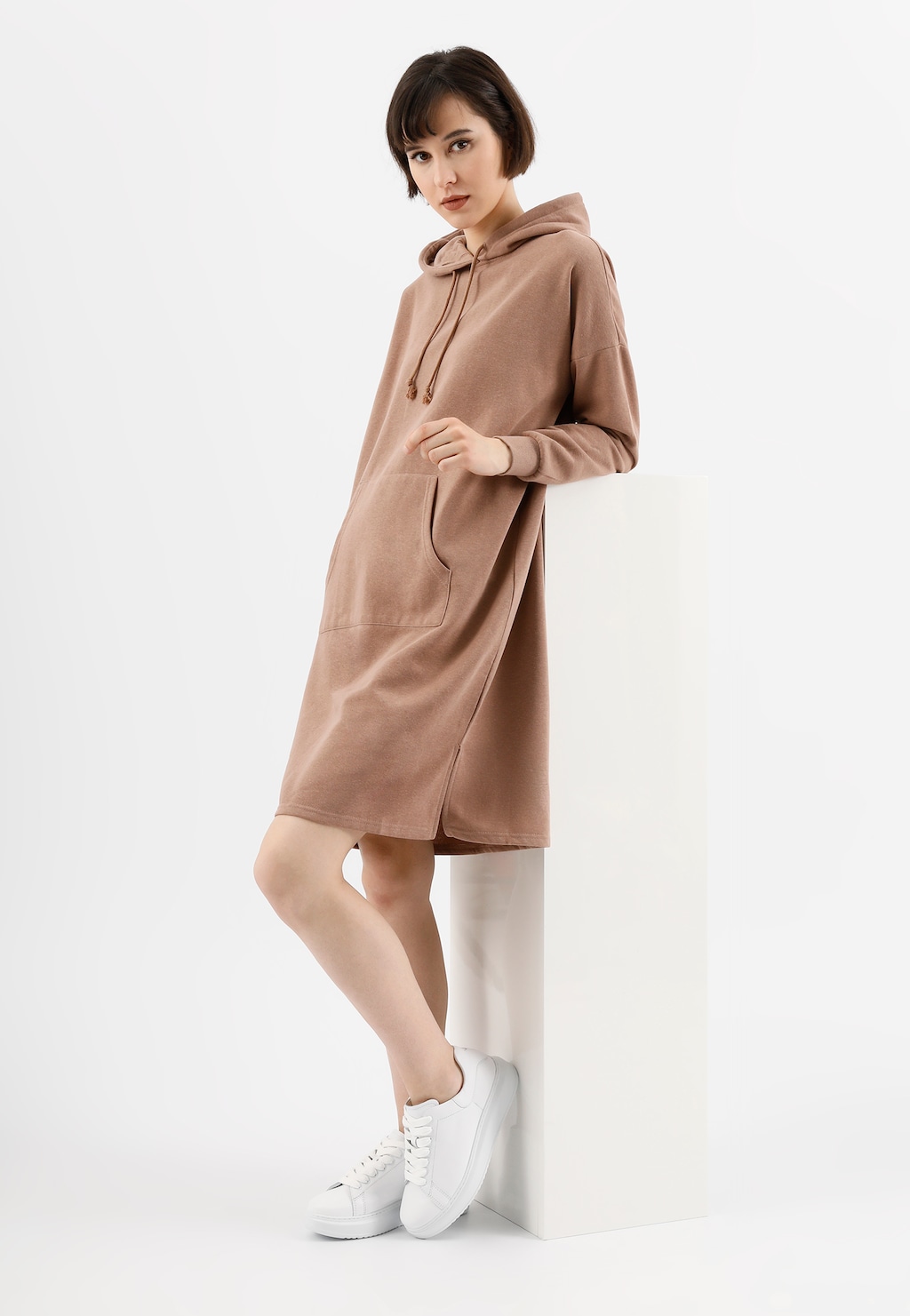 Modelka w beżowej sukience z kapturem, prezentująca klasyczne białe trampki damskie Wojas model 46020-50 ze skóry licowej, idealne do codziennych stylizacji.