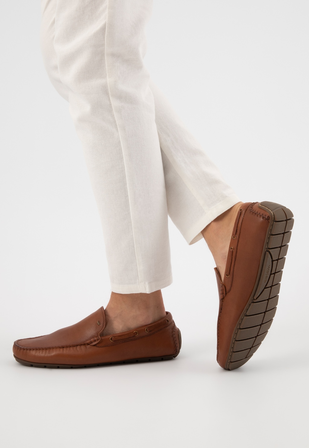 Jasnobrązowe skórzane mokasyny męskie Wojas model 10047-52 prezentowane na nodze w białych spodniach, widoczna wygodna podeszwa i elegancki profil buta.