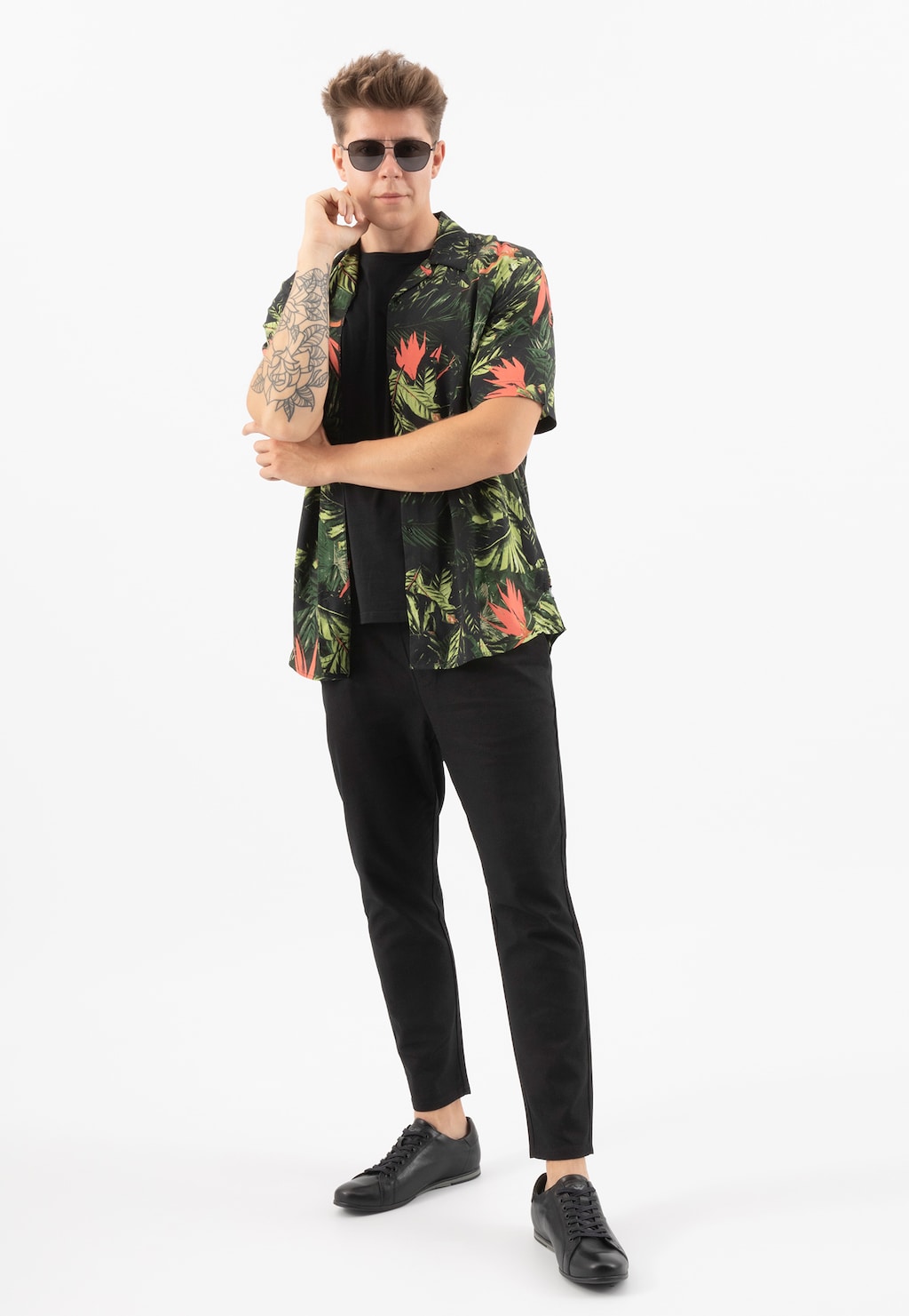 Mężczyzna w hawajskiej koszuli i czarnych spodniach prezentuje czarne minimalistyczne sneakersy Wojas model 8071-51 w klasycznym stylu, idealnie dopełniające casualowy strój.