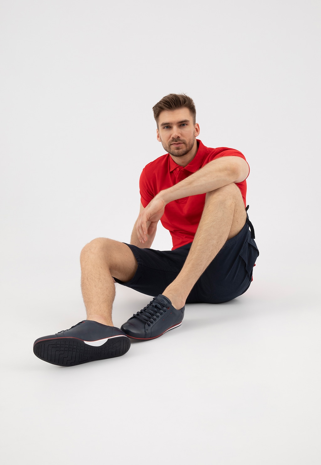 Granatowe półbuty Wojas model 8071-56 z czerwonym akcentem na podeszwie, prezentowane przez mężczyznę w czerwonej koszulce polo i granatowych szortach.