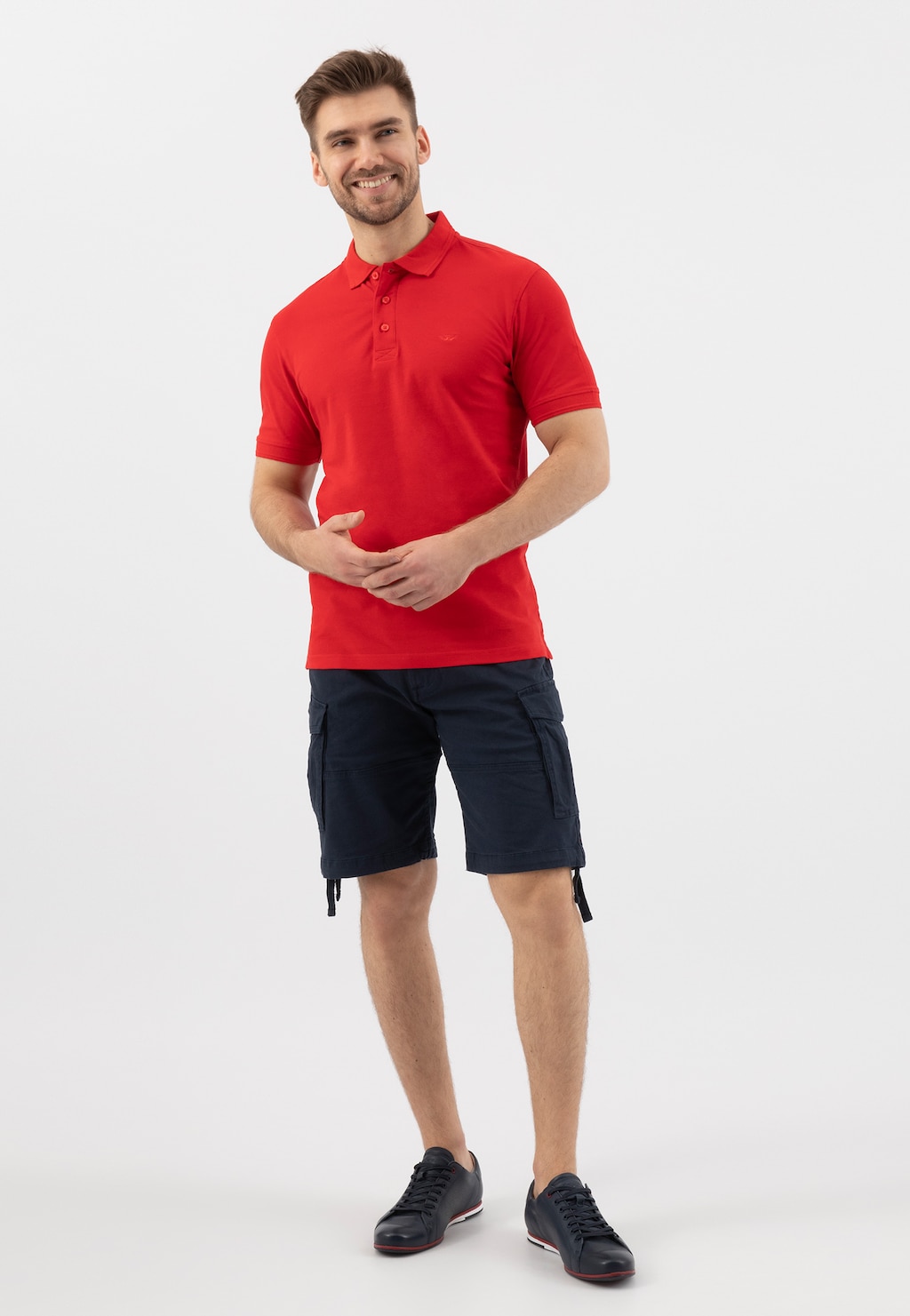 Mężczyzna w czerwonej koszulce polo i granatowych szortach, prezentujący granatowe półbuty Wojas model 8071-56 z charakterystycznym czerwonym akcentem na podeszwie.