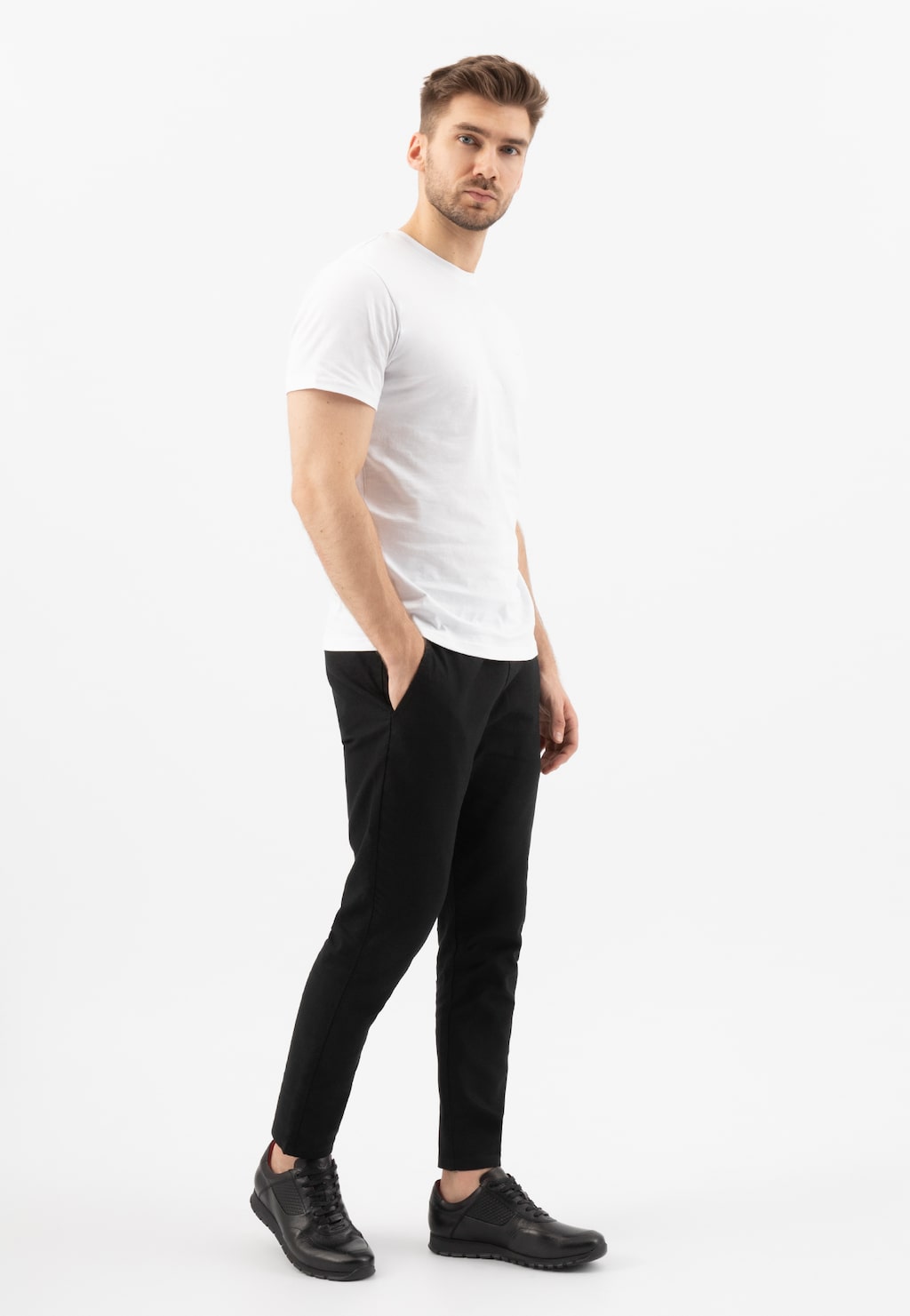 Mężczyzna w białej koszulce i czarnych spodniach, prezentujący czarne skórzane półbuty Wojas model 9078-51 typu sneakers, ukazane z boku w pełnej stylizacji.