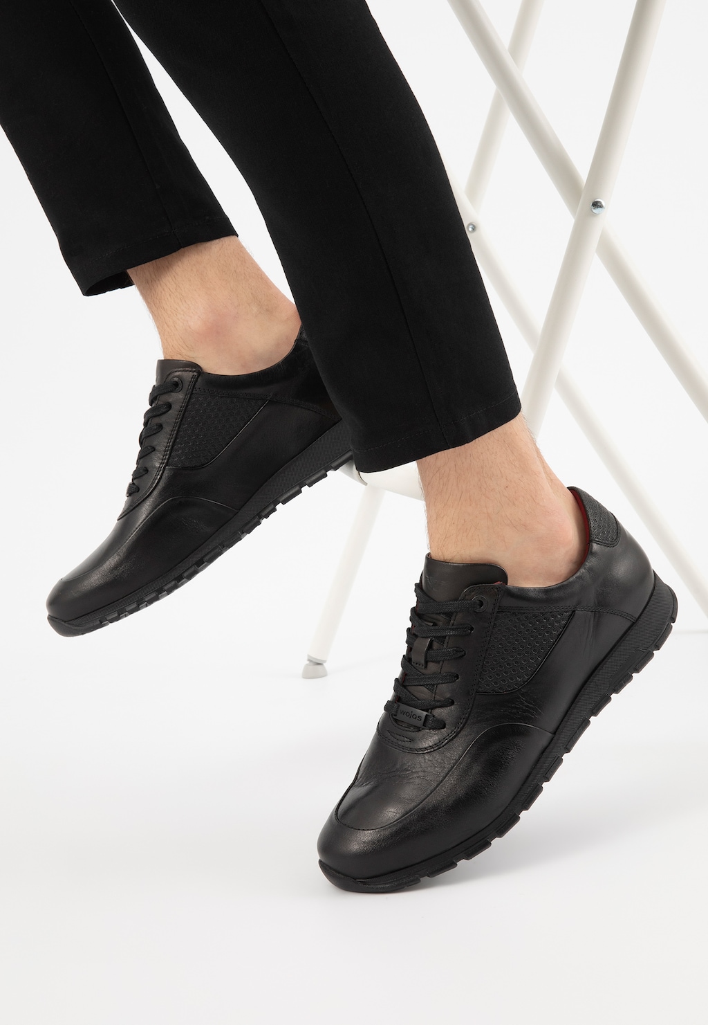 Czarne skórzane półbuty męskie Wojas model 9078-51 typu sneakers, prezentowane na nodze w czarnych spodniach, z widocznym perforowanym detalem na boku.