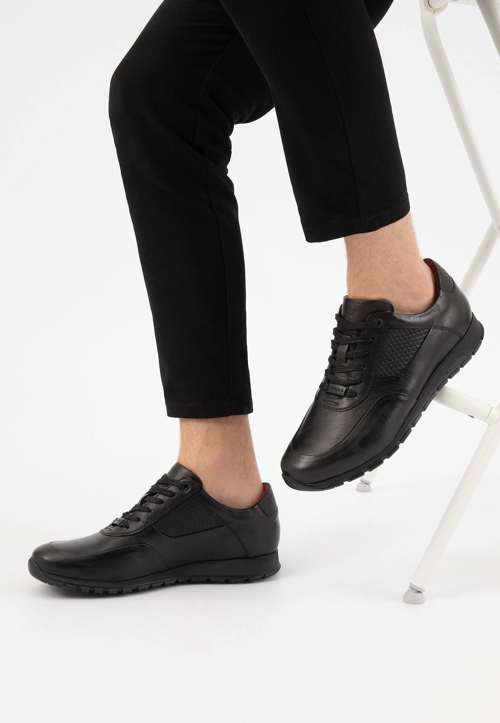 Czarne skórzane półbuty męskie Wojas model 9078-51 typu sneakers na nodze mężczyzny w ciemnych spodniach, pokazane z boku na jasnym tle.