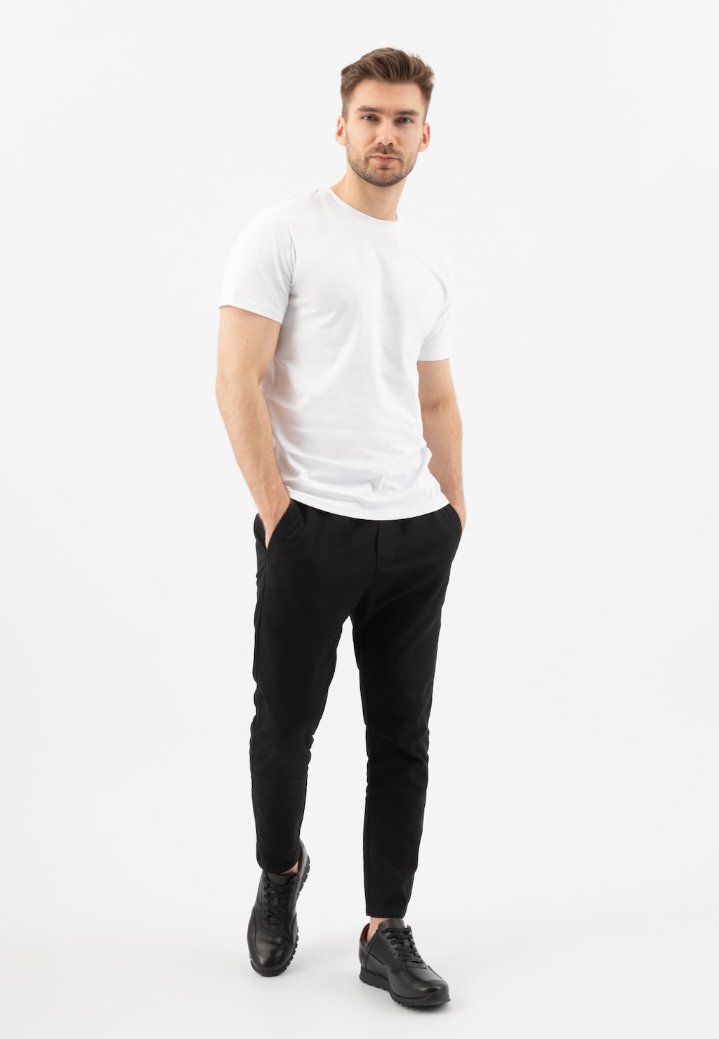 Mężczyzna w białej koszulce i czarnych spodniach prezentuje czarne skórzane półbuty męskie Wojas model 9078-51 typu sneakers, idealne do codziennych stylizacji.