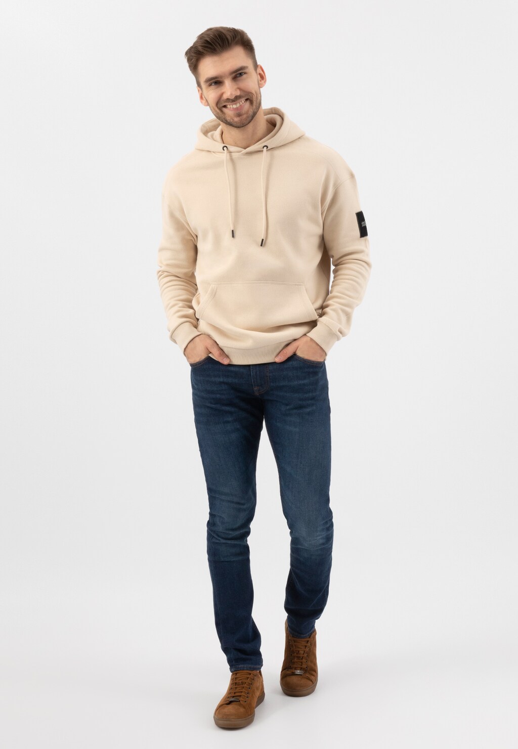 Mężczyzna w beżowej bluzie z kapturem i granatowych dżinsach, prezentujący jasnobrązowe trampki Wojas model 9060-63 z dwoiny welurowej.