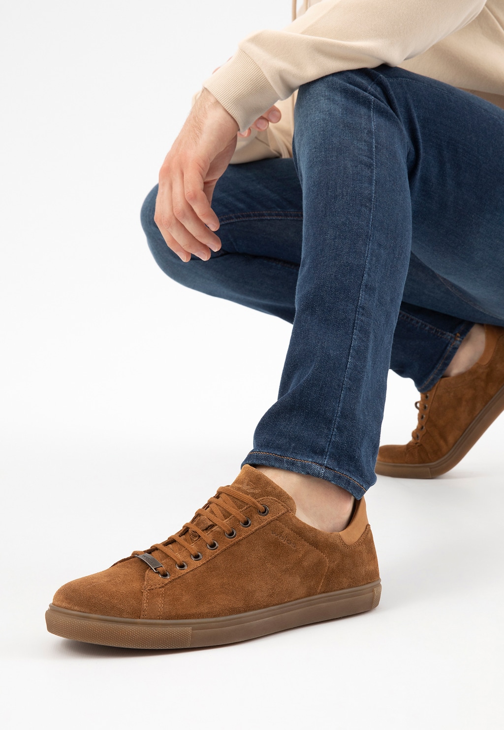 Jasnobrązowe trampki męskie Wojas model 9060-63 z dwoiny welurowej na stopie osoby w jeansach, prezentowane z boku w pozycji kucającej.