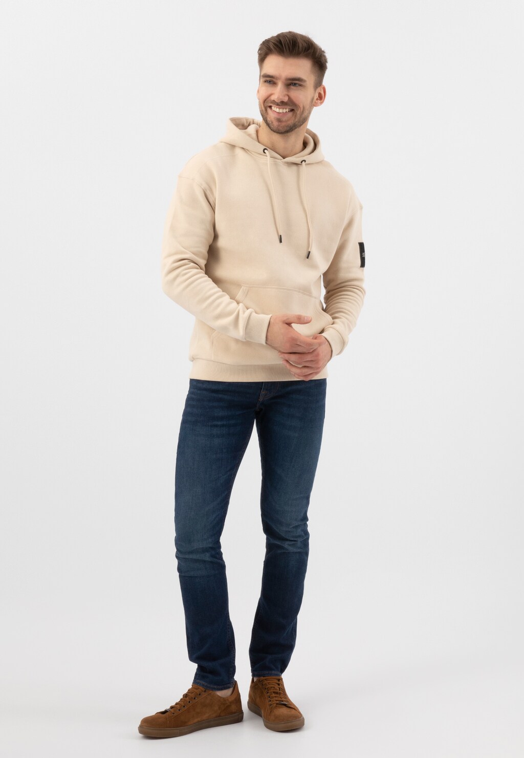 Mężczyzna w beżowej bluzie z kapturem i granatowych jeansach, prezentujący jasnobrązowe trampki męskie Wojas model 9060-63 z dwoiny welurowej.