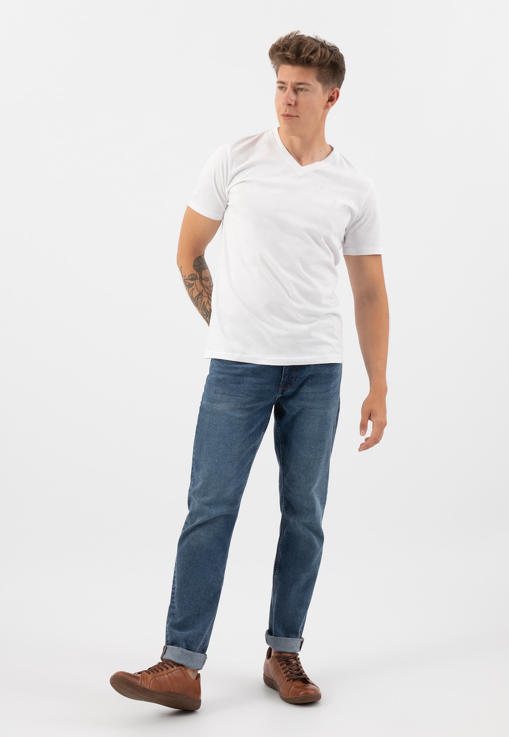 Młody mężczyzna w białej koszulce i jeansach, prezentujący jasnobrązowe półbuty męskie Wojas model 9080-53 z charakterystycznymi przeszyciami, widoczne z pełnej perspektywy.