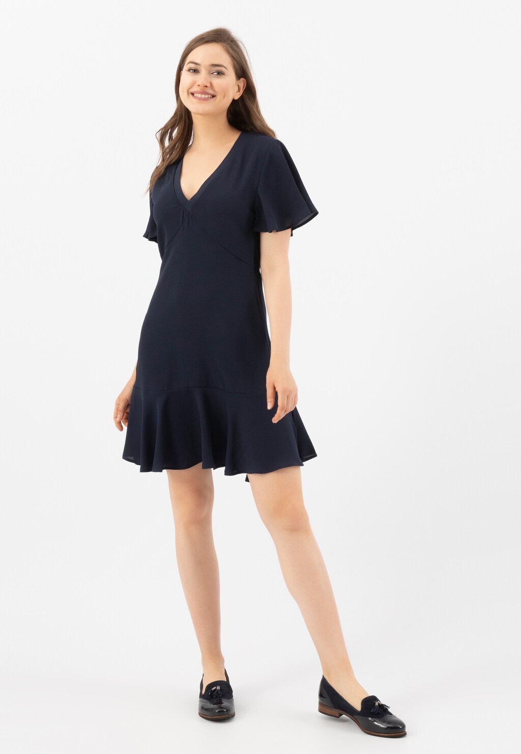 Modelka w granatowej sukience z dekoltem V prezentuje granatowe lordsy damskie Wojas model 46039-76 - eleganckie wsuwane buty idealnie dopełniające stylizację.