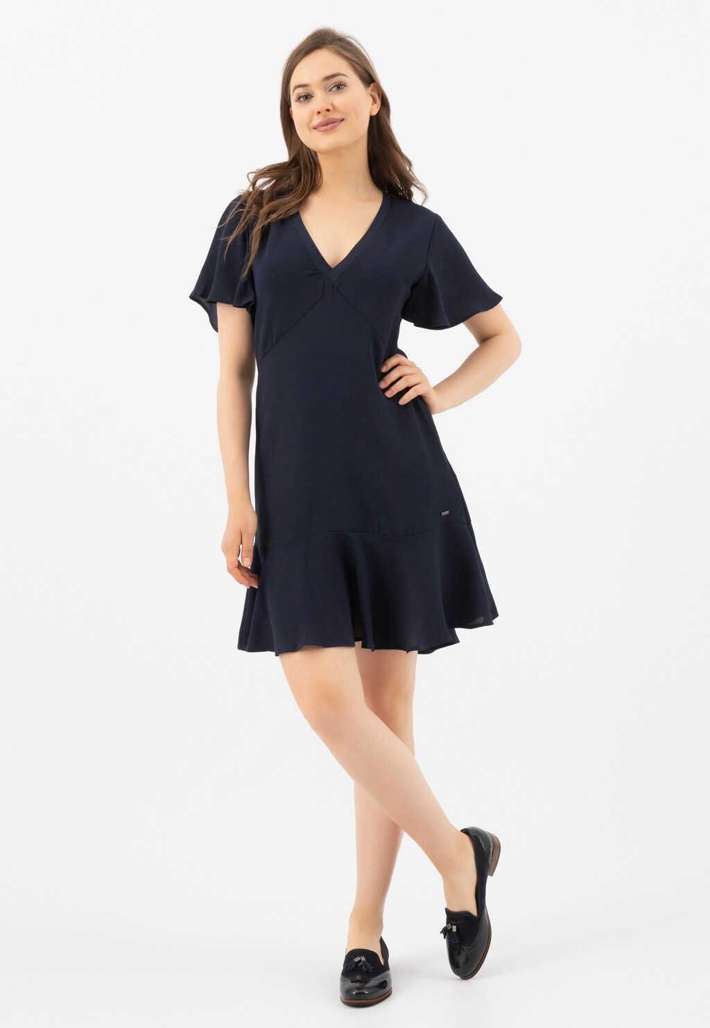 Modelka w granatowej sukience prezentująca granatowe wsuwane lordsy damskie Wojas model 46039-76, widoczne na stopach. Eleganckie połączenie na jasnym tle.