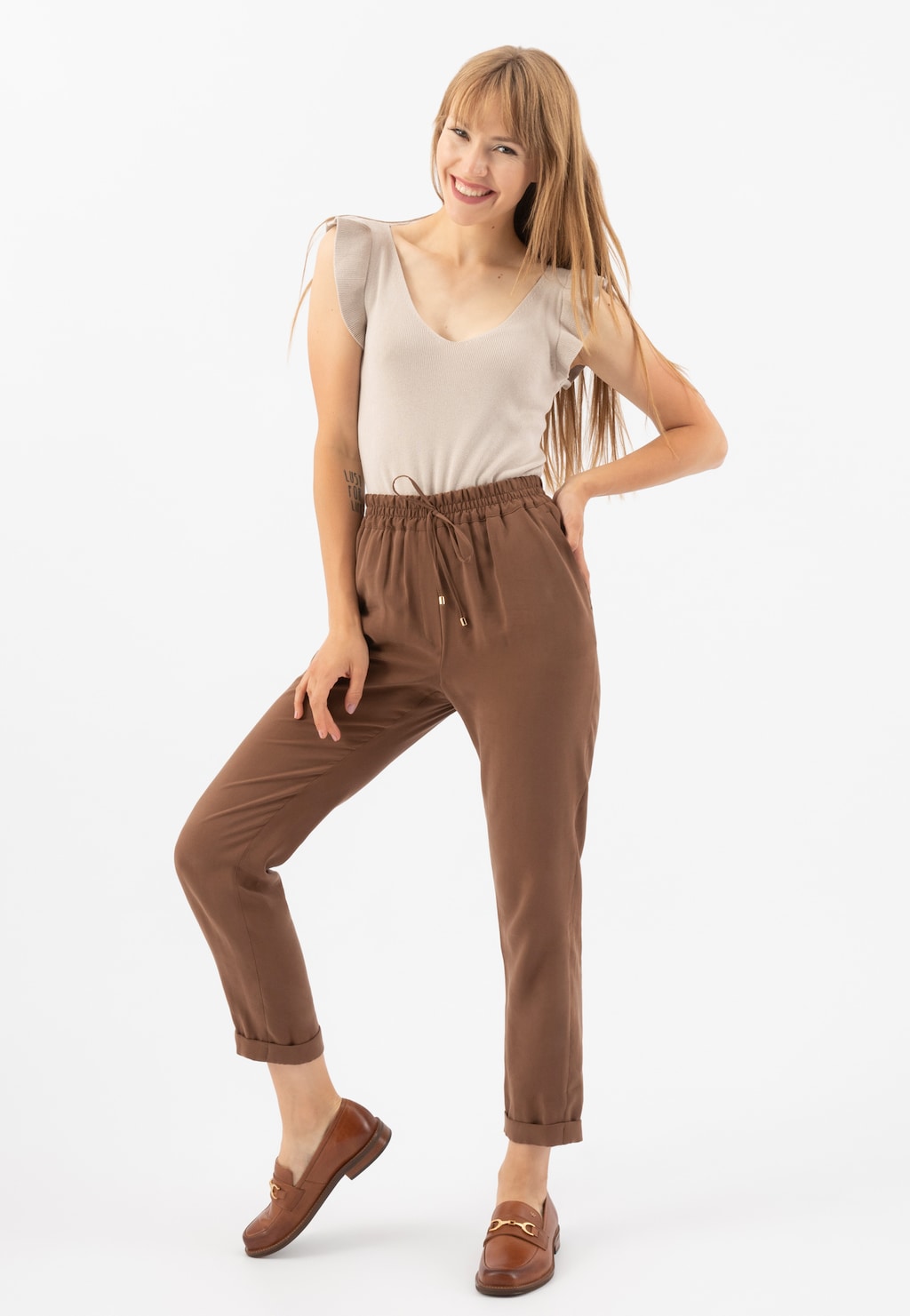 Kobieta w jasnej bluzce i brązowych spodniach prezentuje eleganckie jasnobrązowe mokasyny Wojas model 46092-53 ze skóry licowej, ukazując ich styl i dopasowanie do casualowego stroju.