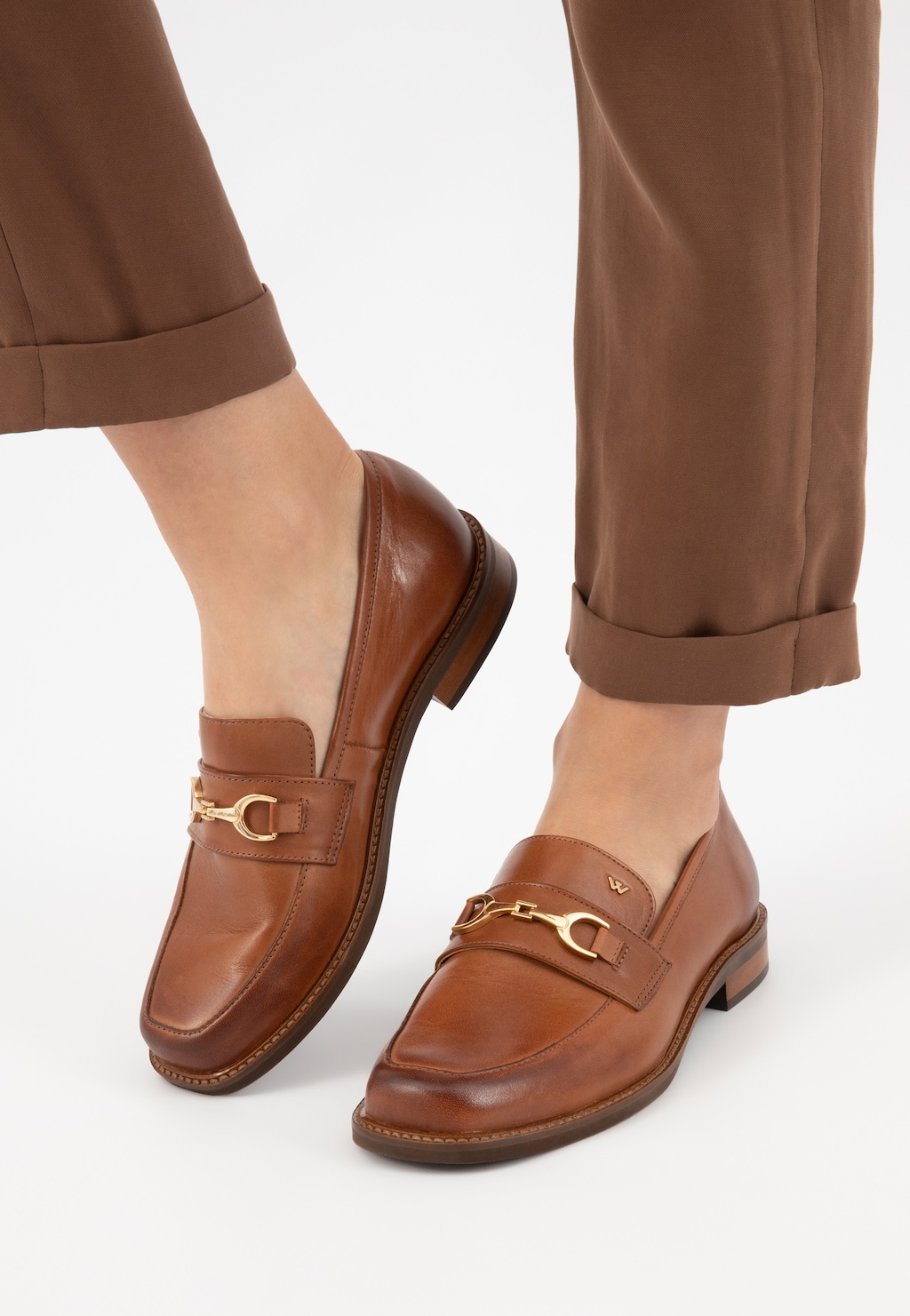 Eleganckie jasnobrązowe mokasyny Wojas model 46092-53 ze złotym elementem na przodzie, noszone z brązowymi spodniami z podwiniętymi nogawkami.