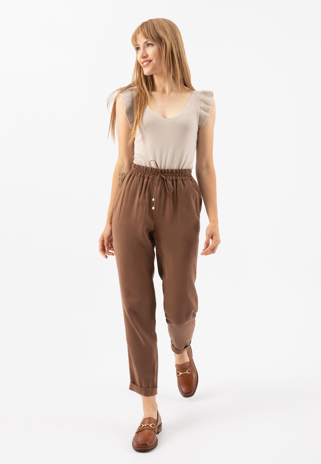 Kobieta w beżowym topie i brązowych spodniach prezentująca eleganckie jasnobrązowe mokasyny Wojas model 46092-53 ze skóry licowej, idealne do casualowych stylizacji.