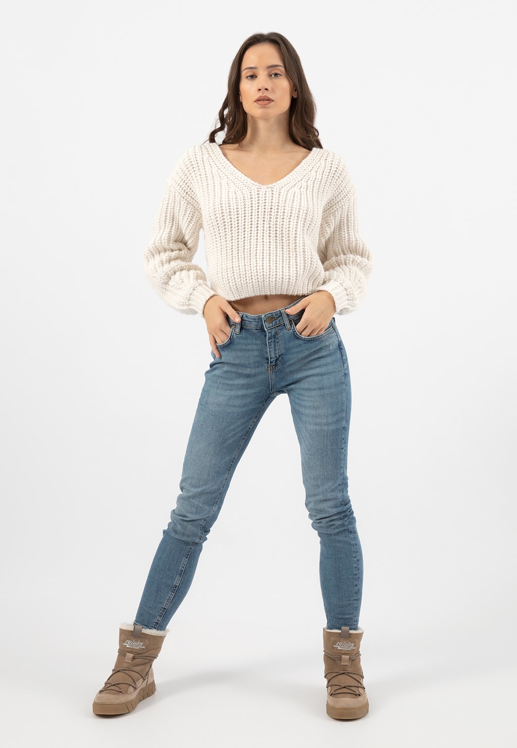 Modelka prezentująca beżowe śniegowce Relaks R55103-74 ocieplane skórą owczą, ubrana w biały sweter i niebieskie jeansy. Buty idealne na zimowe warunki.