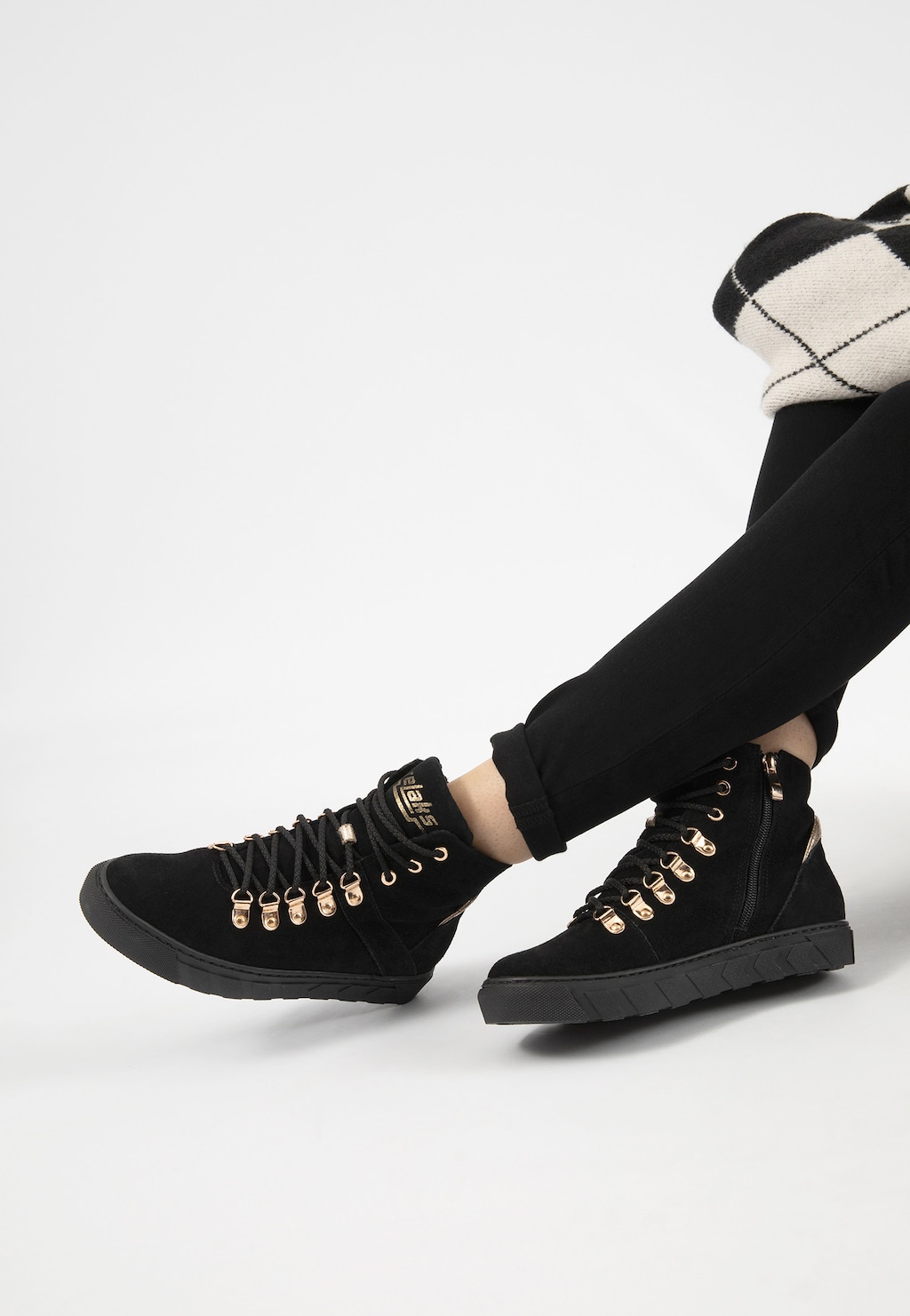 Czarne ocieplane trzewiki damskie Relaks R64006-61 ze złotymi elementami i ozdobnymi sznurowadłami, widoczne na nodze w ciemnych spodniach i biało-czarnej skarpecie.