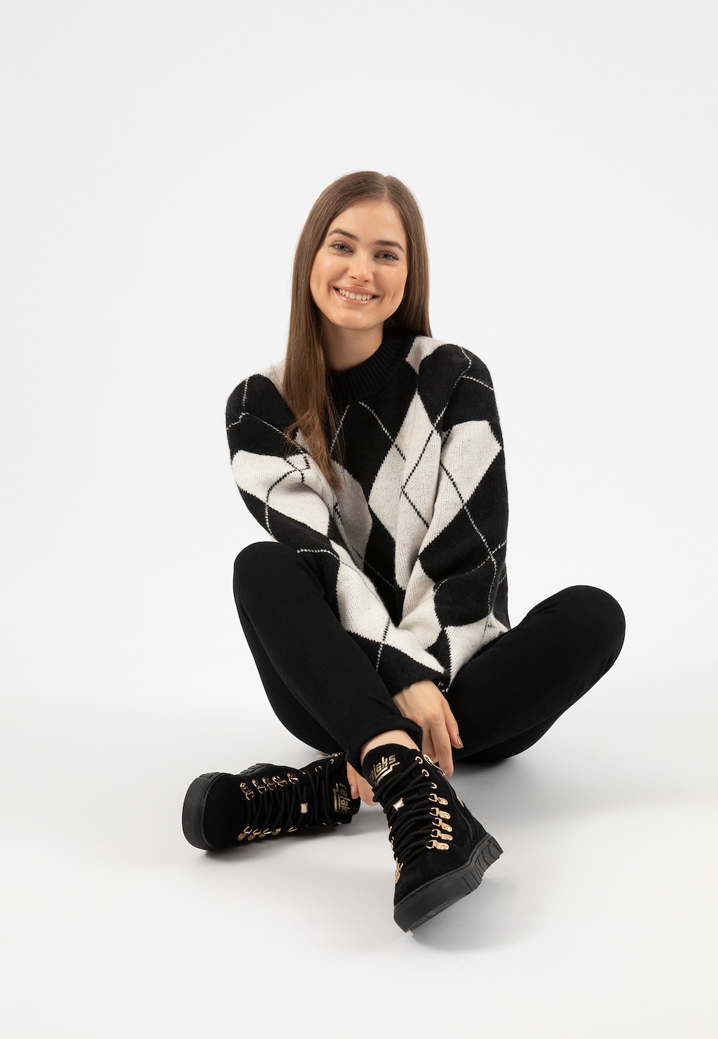 Czarne ocieplane trzewiki damskie Relaks R64006-61 ze złotymi sznurówkami, prezentowane przez modelkę w czarno-białym swetrze w romby i czarnych spodniach.