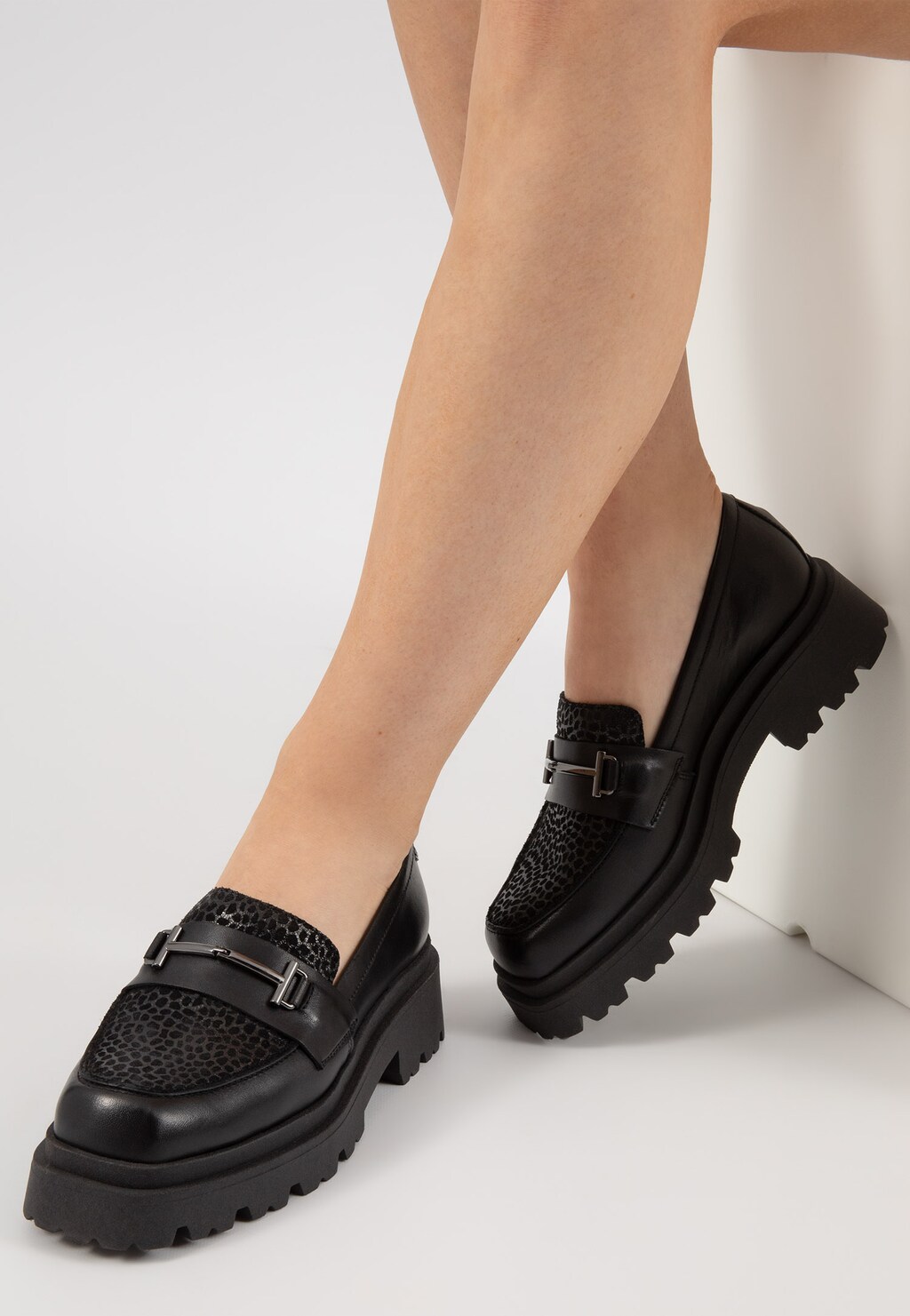 Czarne damskie mokasyny Wojas model 46188-71 z ozdobnym motywem w cętki i metalowym elementem horsebit, na grubej podeszwie, prezentowane na nogach modelki.