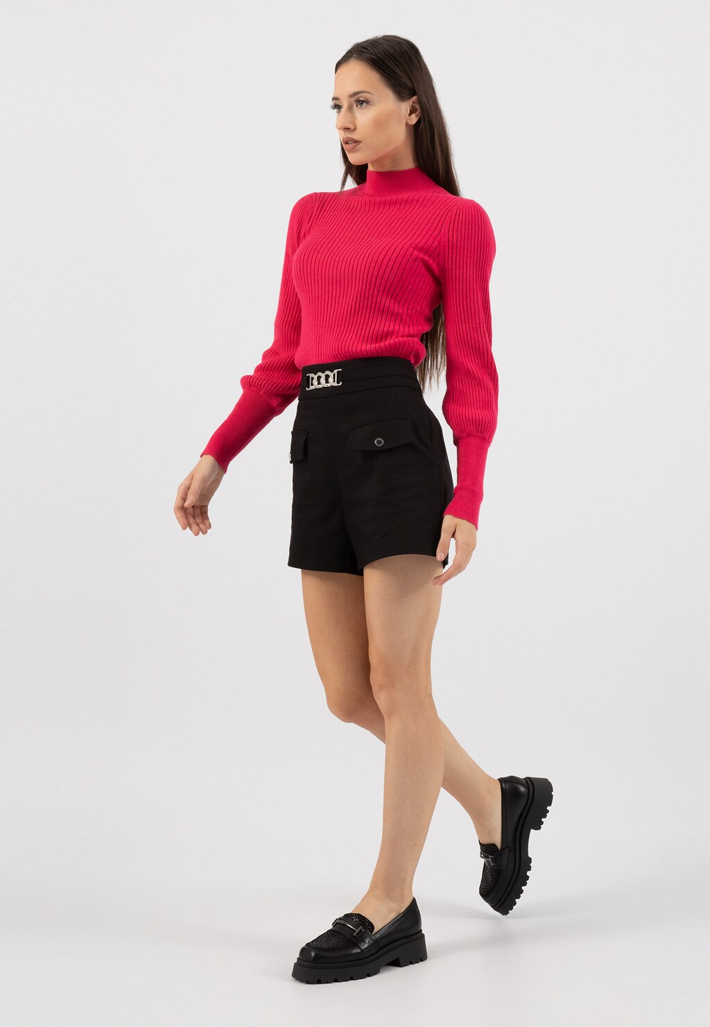 Modelka w różowym swetrze i czarnych szortach prezentuje czarne mokasyny Wojas model 46188-71 z ozdobnym motywem w cętki i elementem horsebit.