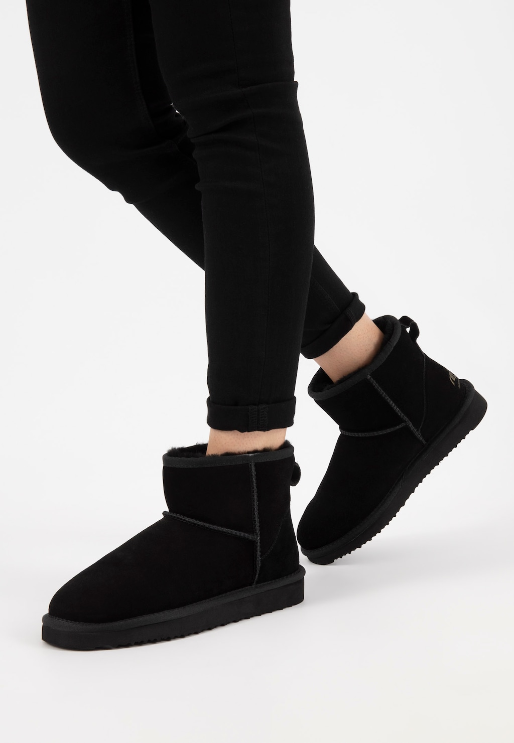 Czarne damskie śniegowce Relaks R55003-61 prezentowane na modelce w czarnych spodniach, widok z boku ukazujący krótkie buty z ciepłym ociepleniem.
