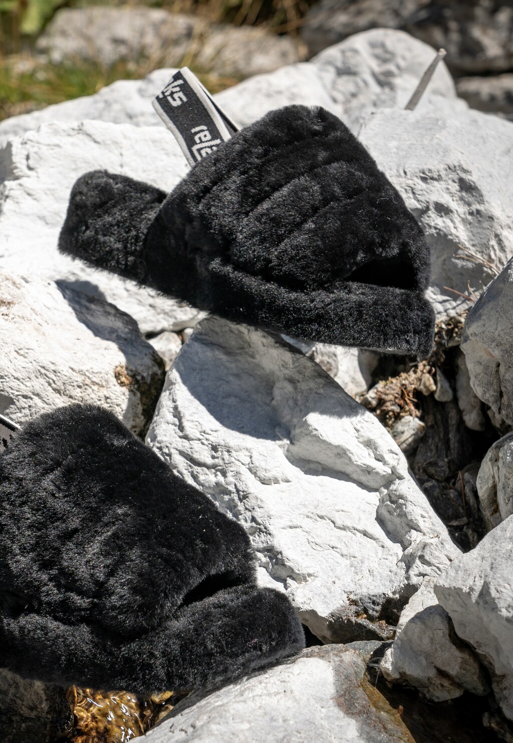 Czarne puchate kapcie Relaks R34006-61 z gumką na piętę sfotografowane na kamiennym podłożu w naturalnym świetle, widoczna metka marki.