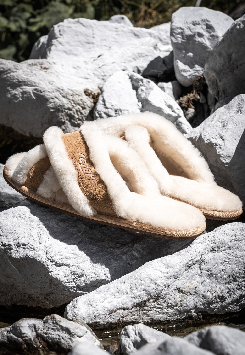 Beżowe puchate pantofle damskie RELAKS model R34005-64 z miękkim futerkiem, sfotografowane na naturalnych skałach, widok z boku.