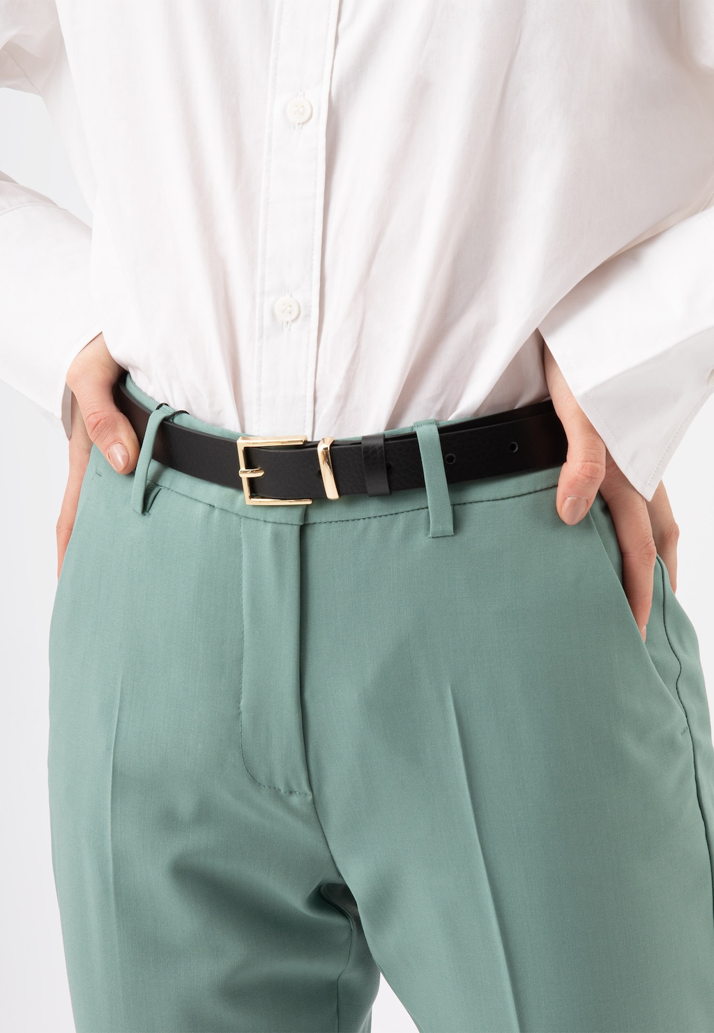 Czarny skórzany pasek damski Wojas 93071-51 ze złotą klamrą, elegancko noszony z białą koszulą i miętowymi spodniami, widok z przodu na talii.