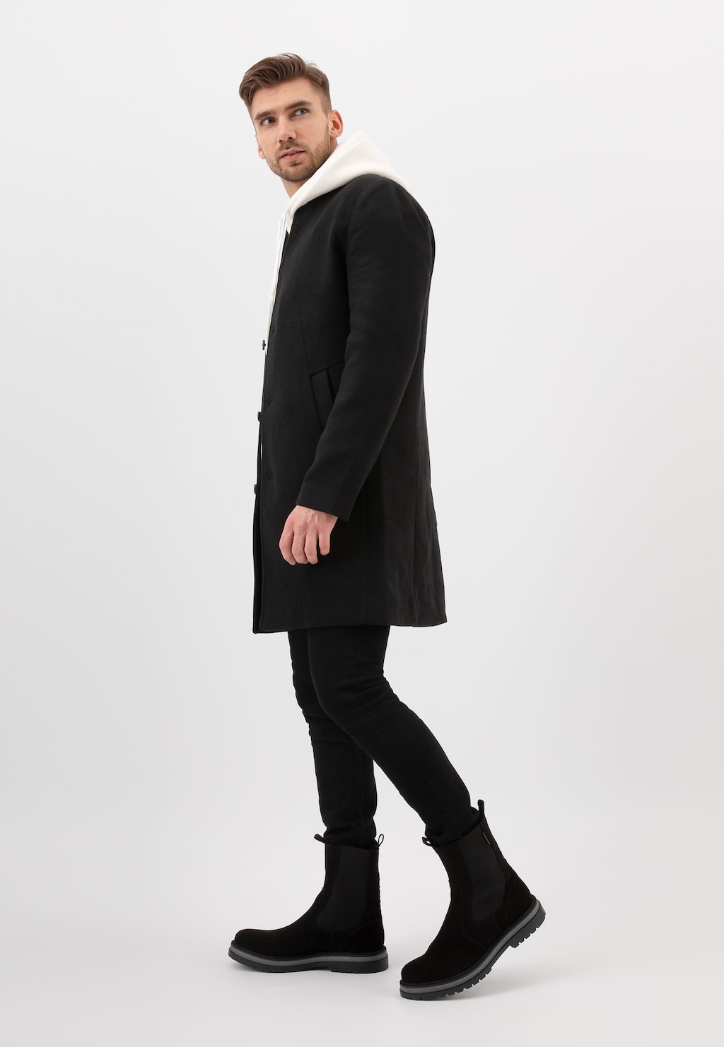 Mężczyzna w czarnym płaszczu i spodniach, prezentujący czarne sztyblety męskie Wojas z wysoką cholewką, model 20021-61, widoczne z bocznej perspektywy.