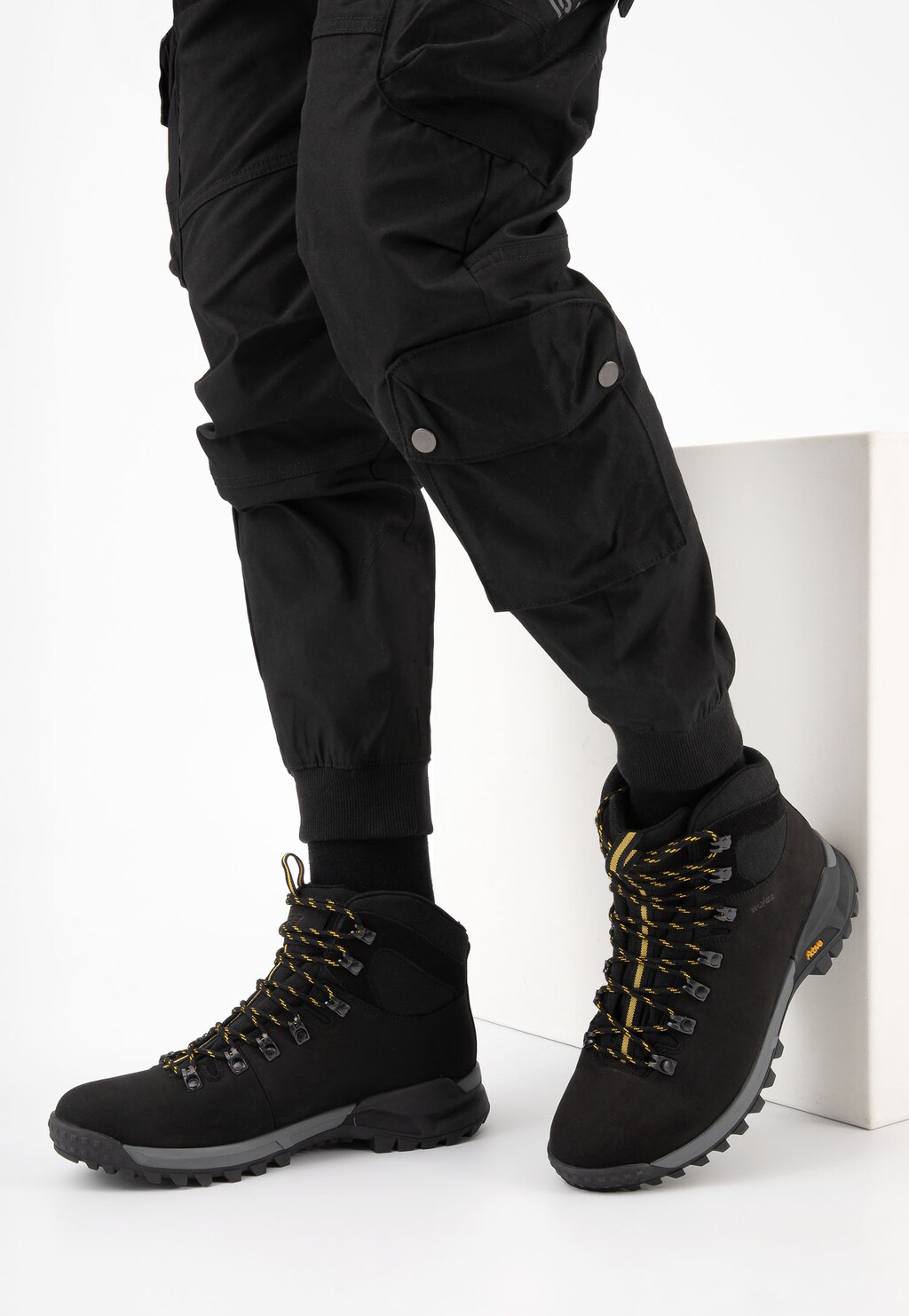 Czarne trzewiki trekkingowe Wojas model 24028-71 z żółtymi sznurówkami, prezentowane na nodze w czarnych spodniach cargo, widok z boku.